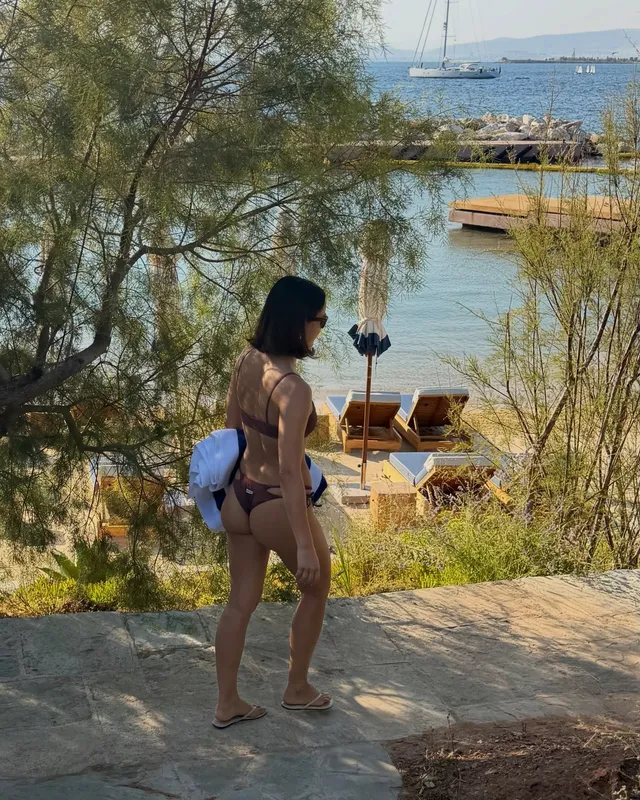 Camila Mendes standing by a coastal path in sandals.