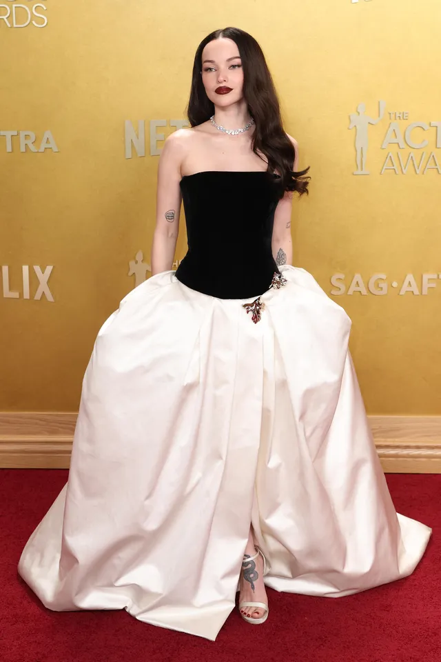 Dove Cameron posing in a black-and-white gown and metallic heels.