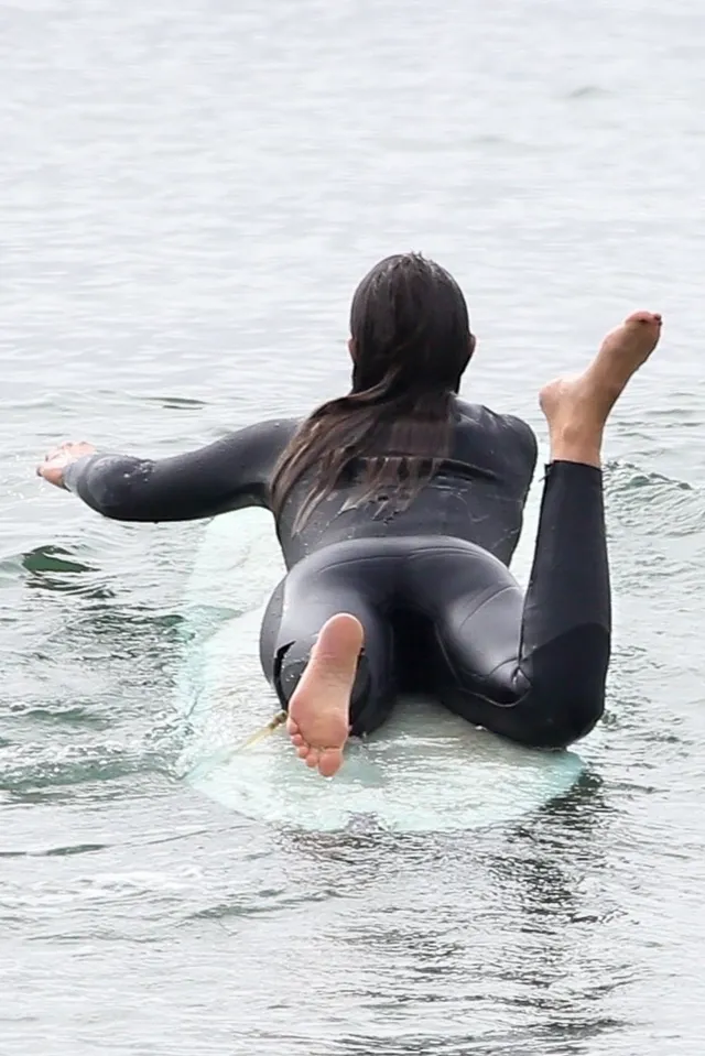 Leighton Meester lying on a surfboard facing out to sea.