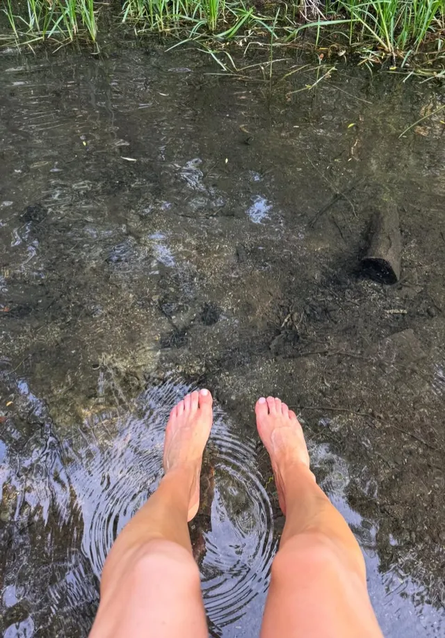Ellie Goulding resting bare feet in shallow water.