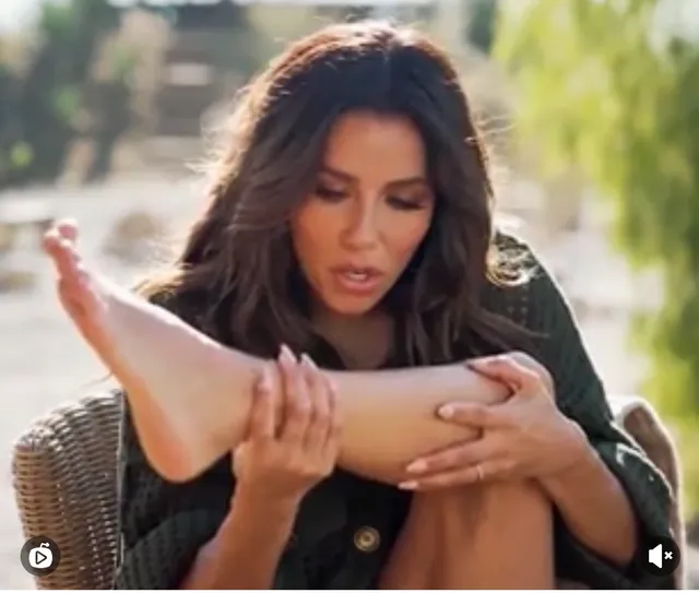 Eva Longoria holding a bare foot while seated outside.
