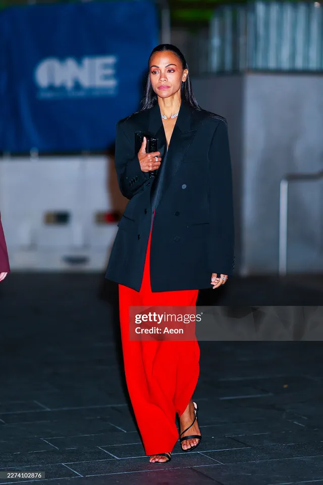Zoe Saldaña walking outside in a red skirt and black sandals.