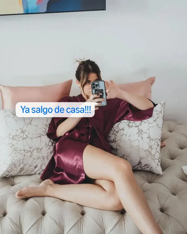 Nicole Wallace taking a mirror selfie while reclining barefoot in a satin dress.