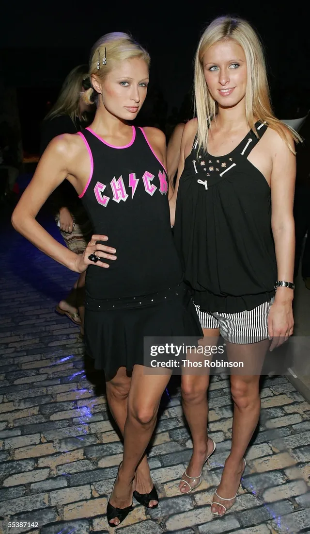 Paris Hilton standing beside a companion in a black outfit and heels.