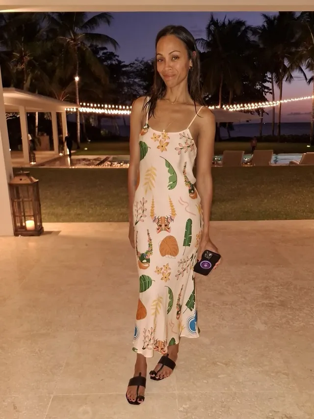 Zoe Saldaña standing outdoors in a printed pale dress.