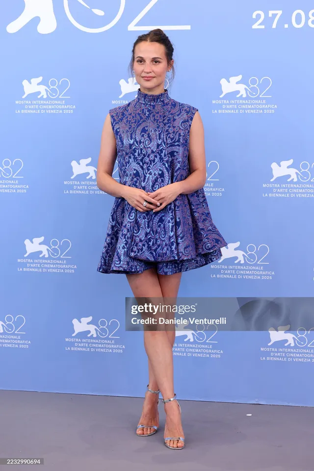 Alicia Vikander posing at a festival in a blue patterned minidress.