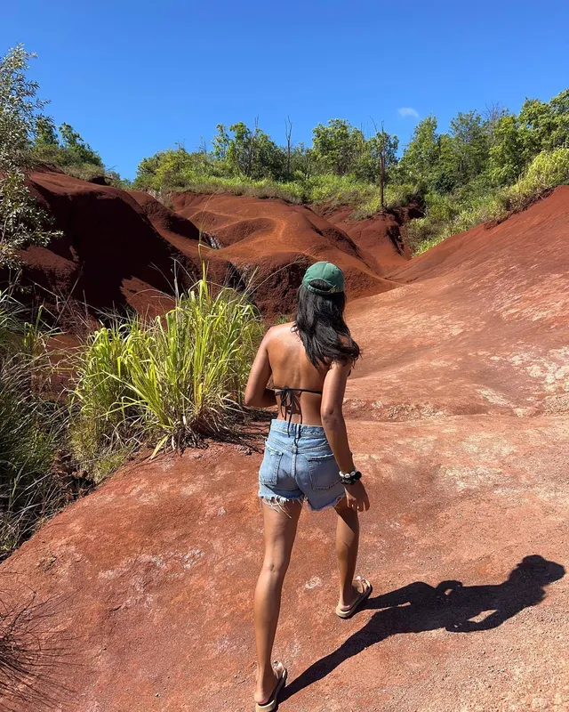 Greta Onieogou walking on a red dirt path in denim shorts and flat sandals.