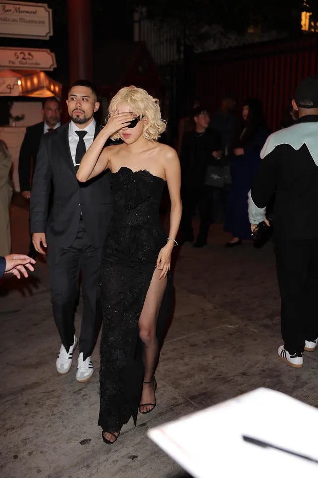 Rosé leaving an entrance at night in sunglasses, a black gown and ankle-strap heels.