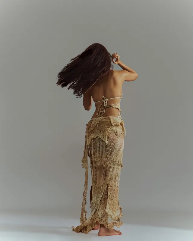 Disha Patani standing barefoot in a fringed gold outfit with her hair moving.