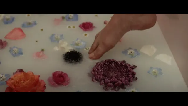 Cailee Spaeny raising a bare foot above water scattered with flowers.