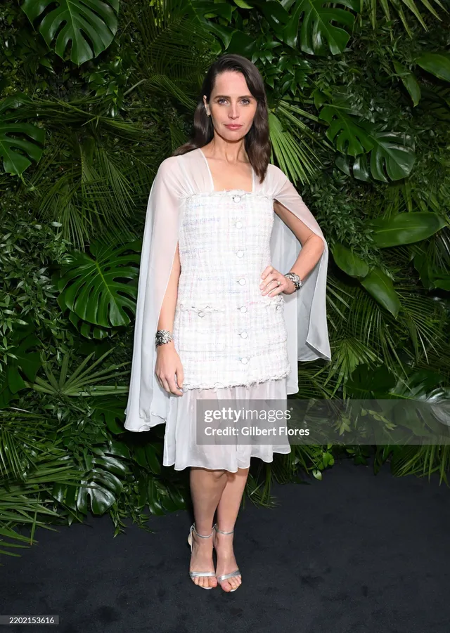 Felicity Jones posing against greenery in a short white dress.