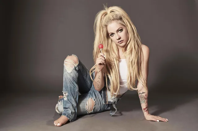 Avril Lavigne sitting barefoot on a studio floor in ripped jeans.