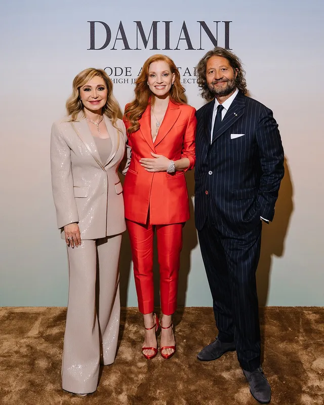 Jessica Chastain posing with two guests in a red suit.