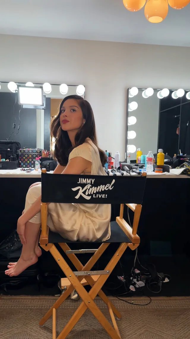 Olivia Rodrigo: seated barefoot in a dressing-room chair.
