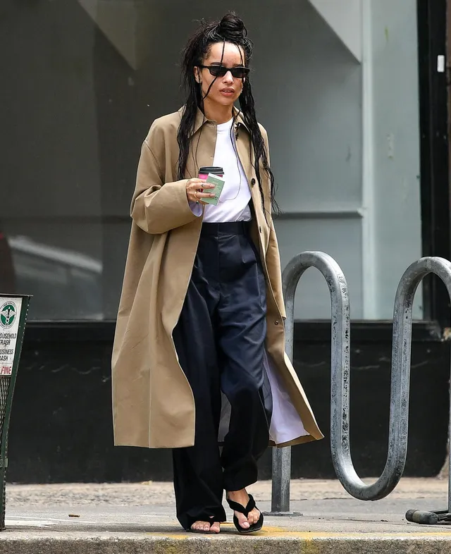 Zoë Kravitz walking in a long coat and flat sandals.