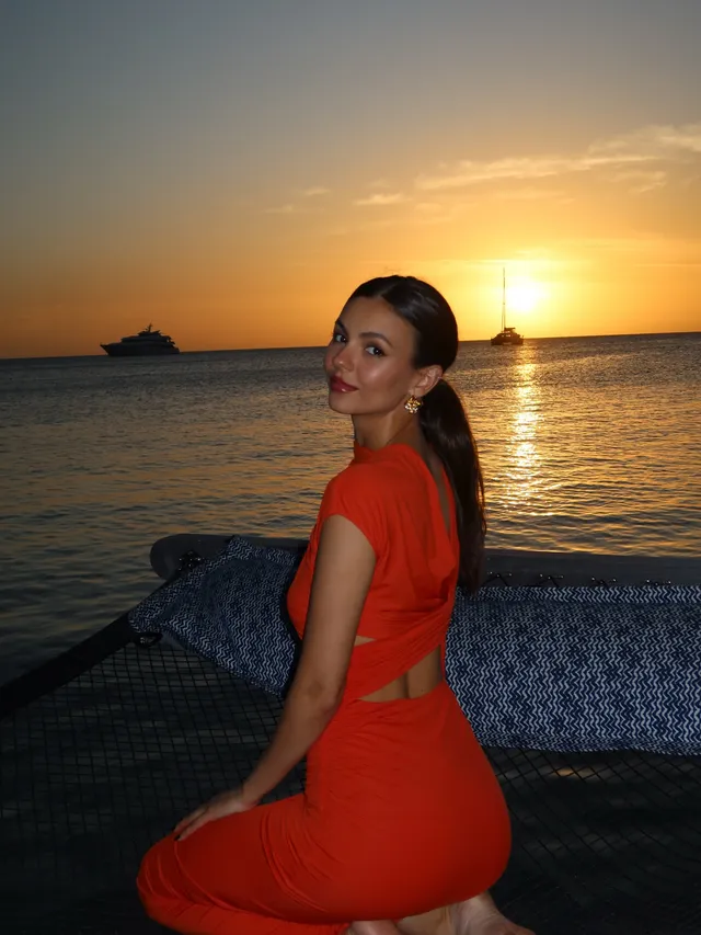Victoria Justice sitting in an orange dress at sunset.