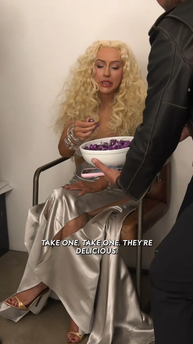 Christina Aguilera sitting in a metallic gown and pale pointed heels.