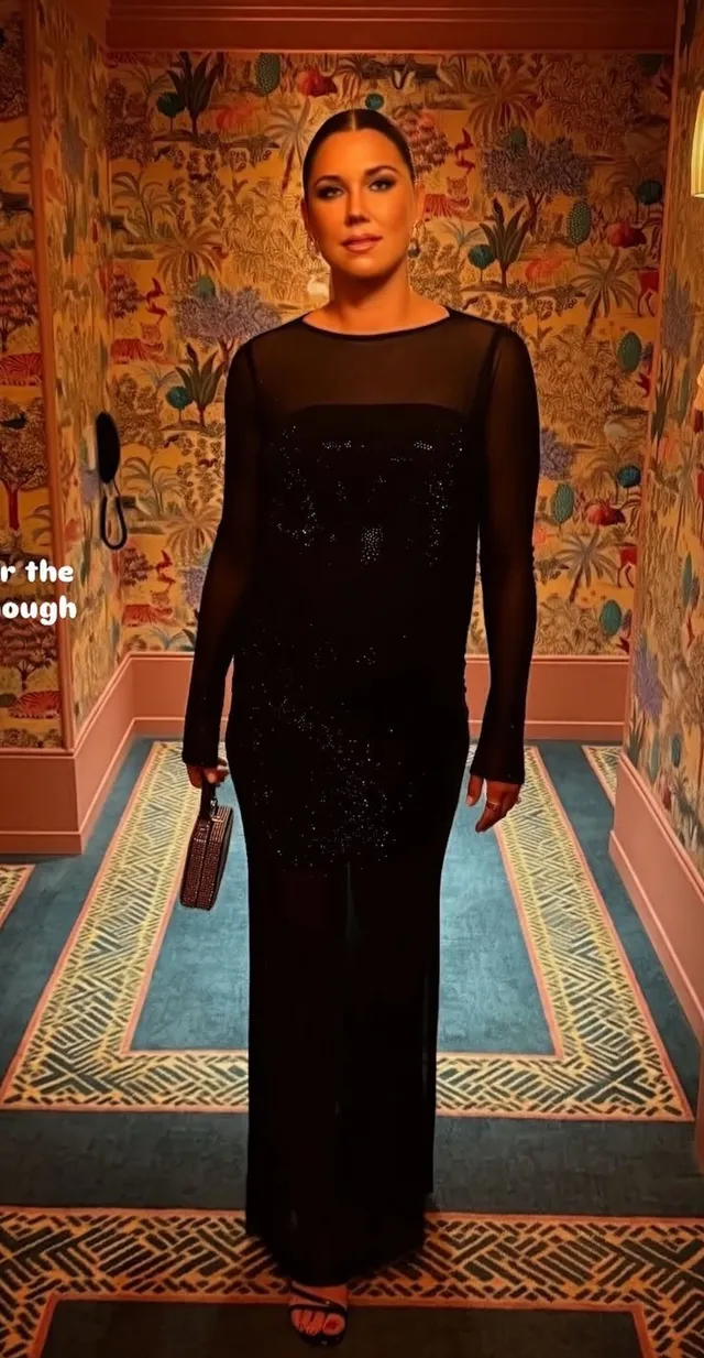 Alex Morgan wearing heels beneath a long dark dress in an ornate room.