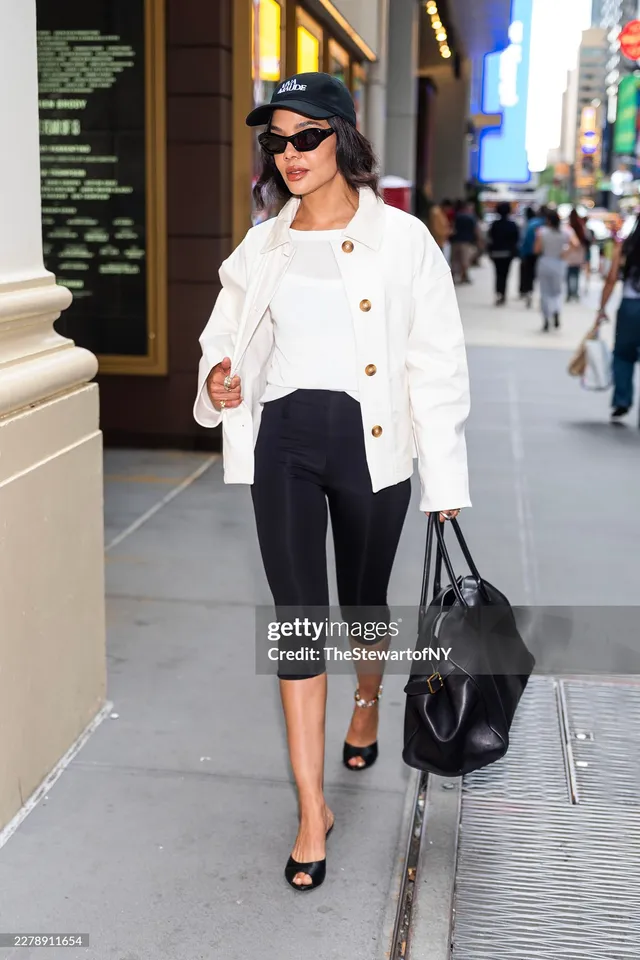 Tessa Thompson walking outside with a dark bag and white jacket.
