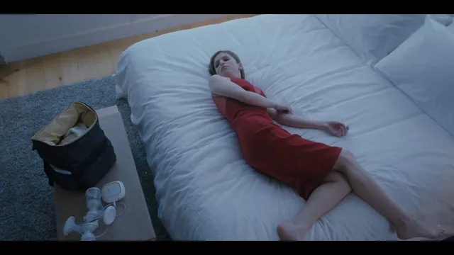 Anna Kendrick lying on a bed in a red skirt with bare feet extended.