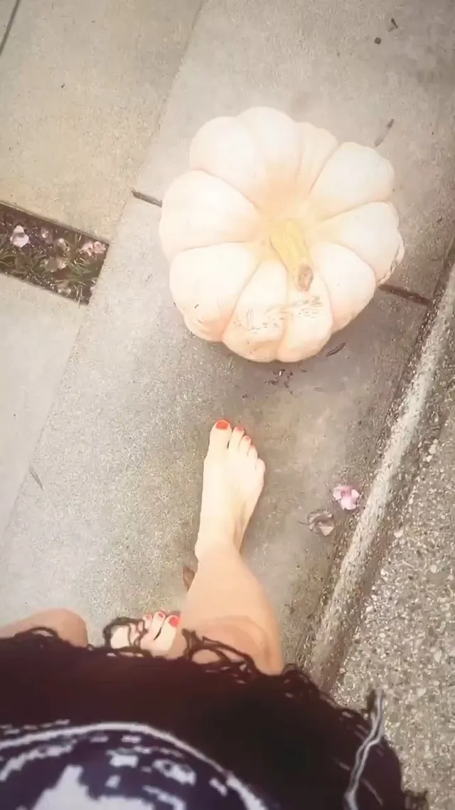 Avril Lavigne standing barefoot beside a pale pumpkin.