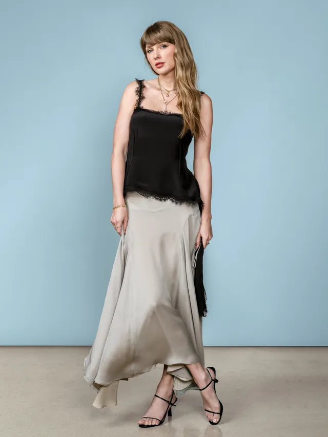 Taylor Swift: standing in a black top, grey skirt and black heels.