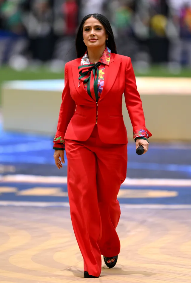 Salma Hayek walking outdoors in a red trouser suit.