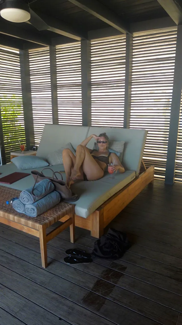 Olivia Holt reclining barefoot on an outdoor sofa in a bikini.