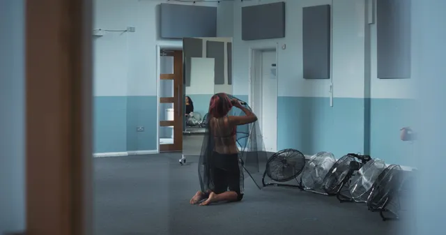 Naomi Scott standing barefoot beside floor fans in a rehearsal room.
