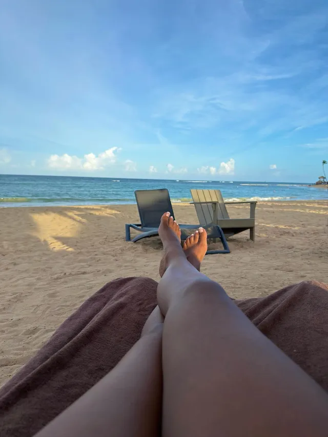 Carlacia Grant reclining barefoot on a beach lounger facing the sea.