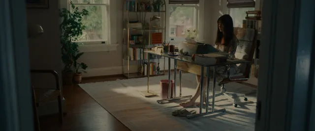Anne Hathaway seated at a dining table in a dimly lit screen scene.