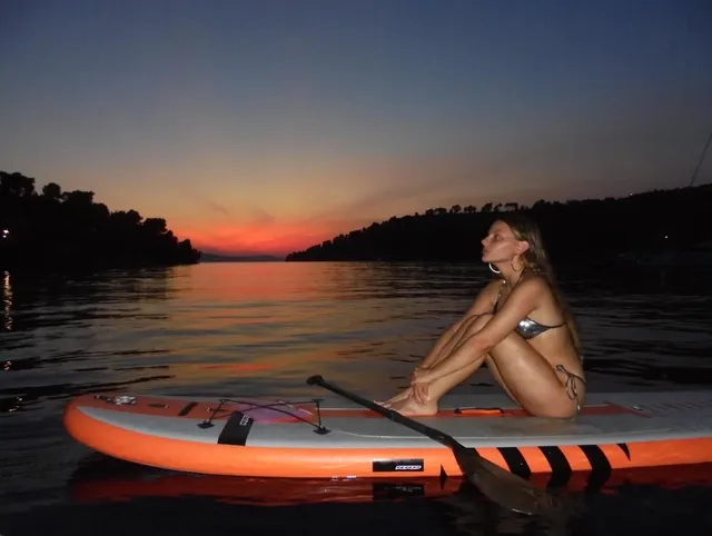 Dafne Keen sitting barefoot on a paddleboard at sunset.