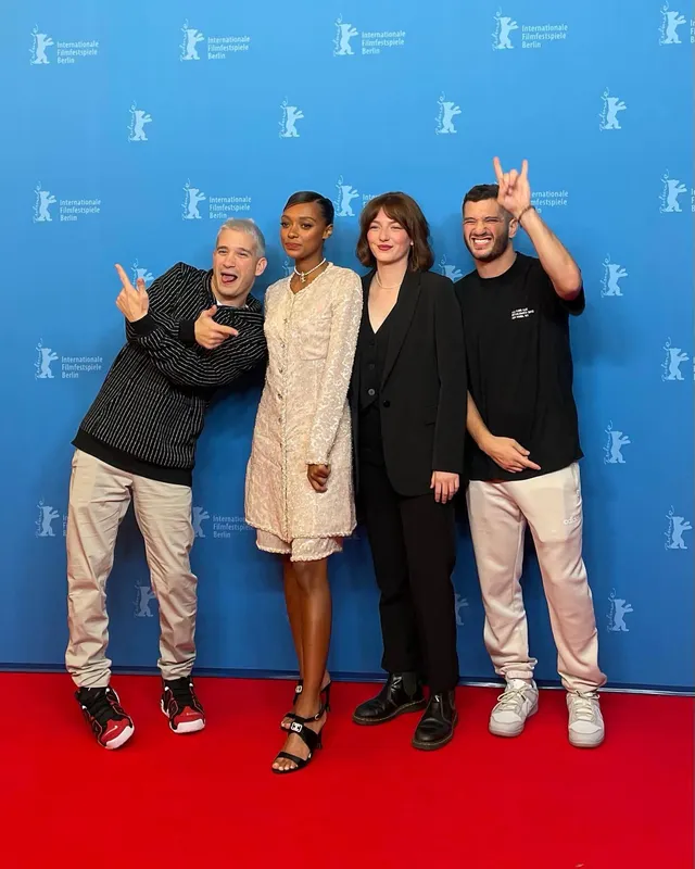 Sophie Wilde posing with three people in a pale dress and black heels.