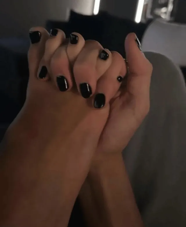 Charli D’Amelio showing black painted toenails and fingernails in a close up.