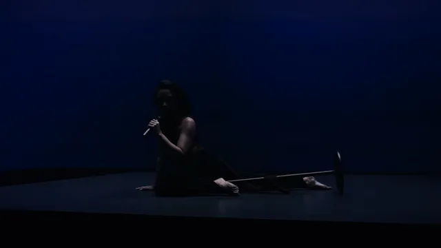 Demi Lovato sitting barefoot beside a microphone in a blue-lit studio setting.