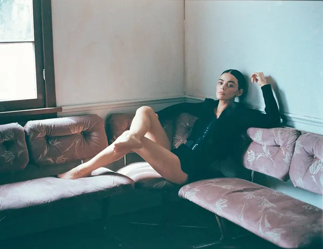 Lucy Hale reclining on a velvet sofa in a black outfit.