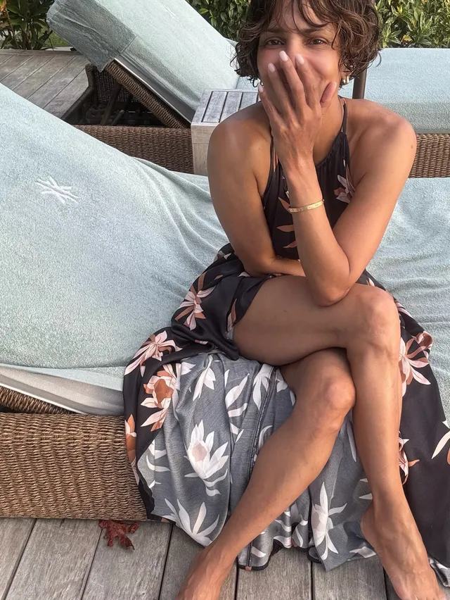 Halle Berry sitting barefoot on an outdoor sofa in a floral dress.