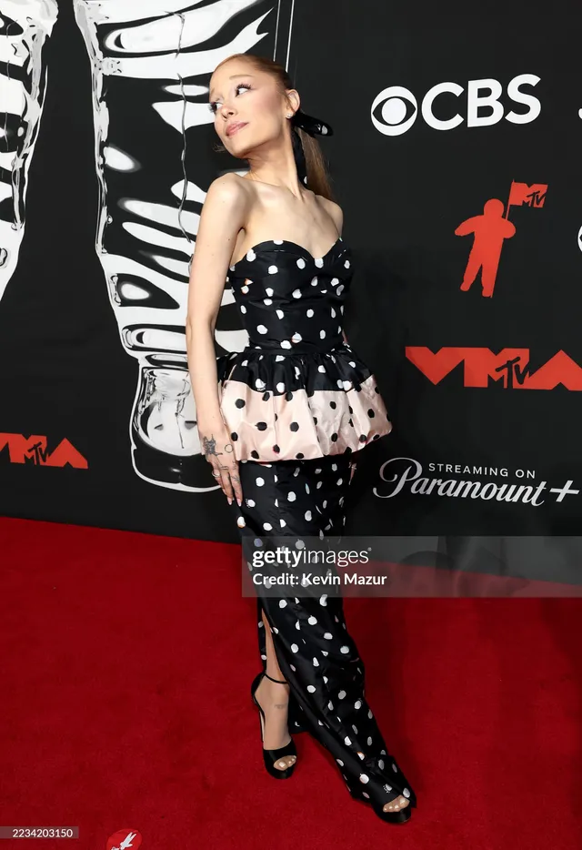 Ariana Grande turning beside an awards backdrop.