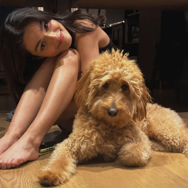 Rachel Zegler sitting barefoot on a wooden floor beside a dog.