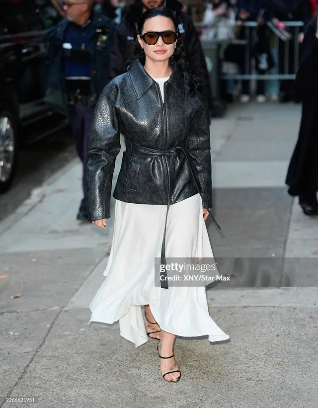 Demi Lovato walking outdoors in a white skirt and strappy heels.