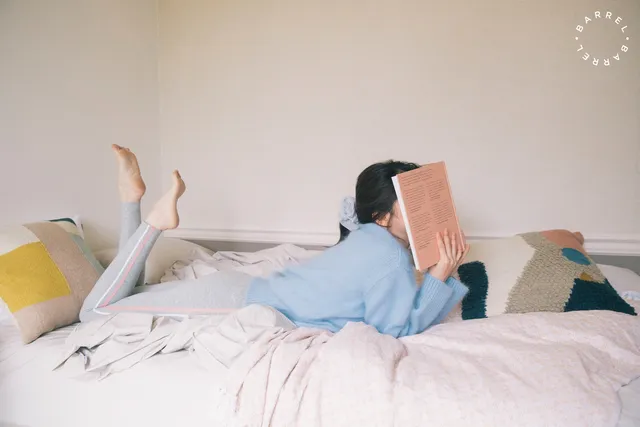 Han So-hee lying barefoot on a bed while reading.