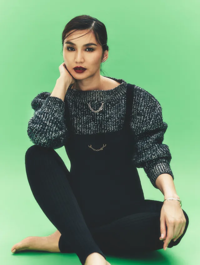 Gemma Chan sitting against a green background in a studio portrait.