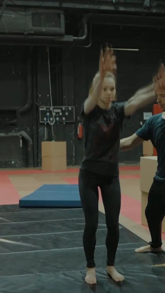 Emma Myers training barefoot with hands raised on a gym mat.