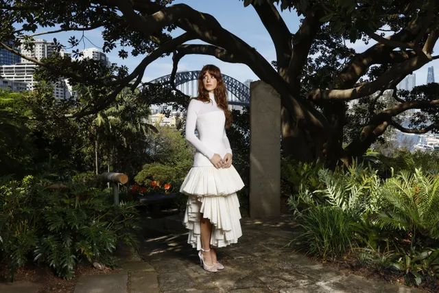 Daisy Edgar-Jones posing in a white dress and heels beside a tree.