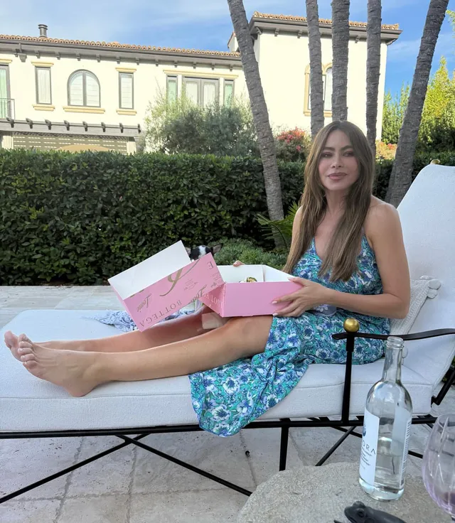 Sofía Vergara reclining on an outdoor lounger in a floral dress with her bare soles visible.