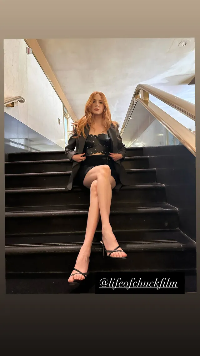 Karen Gillan sitting on a staircase in a dark dress and strappy heels.