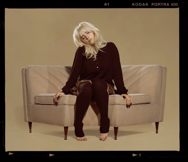 Billie Eilish a seated burgundy outfit with footless tights.