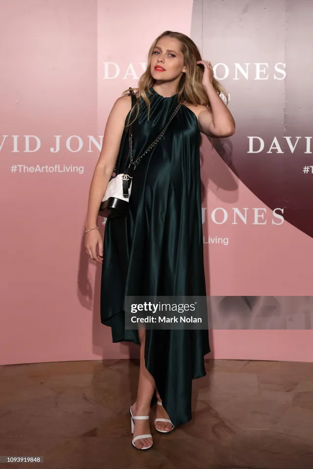 Teresa Palmer posing at an event in a dark satin dress.