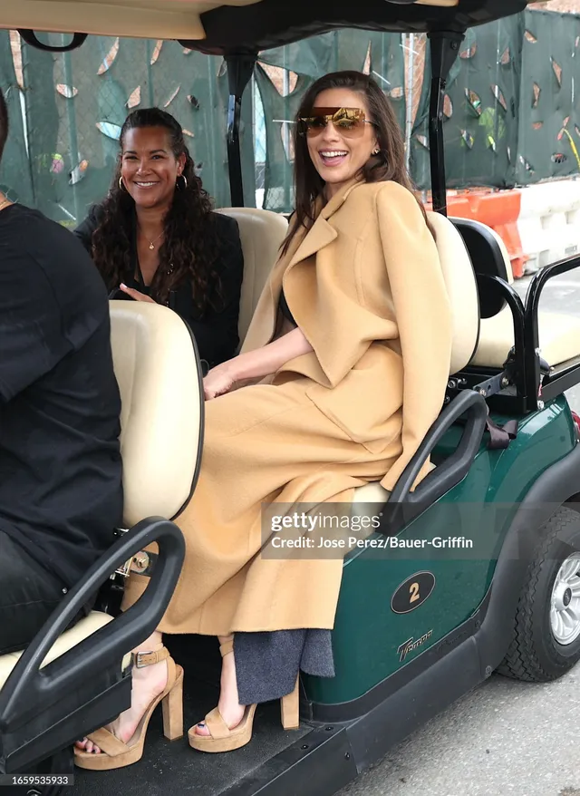 Hayley Atwell sitting on a cart in a camel coat.