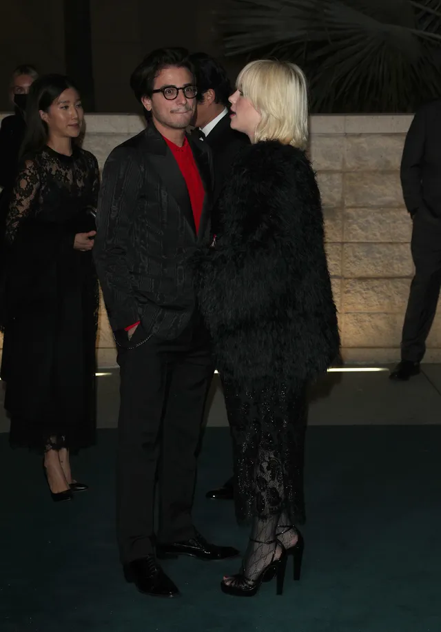 Billie Eilish posing beside another guest in a black dress and heels.